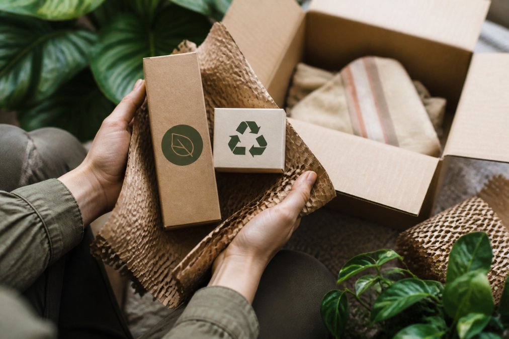 Close-up of hands holding eco-friendly packaging and product boxes with sustainable materials and fair trade labels visible, natural light highlighting the product details