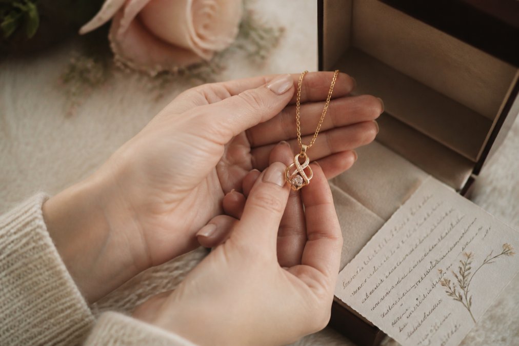 Hands holding a gold pendant necklace with a handwritten note as one of the best anniversary gifts.