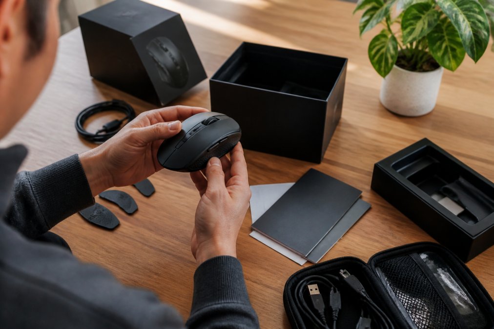 A person's hands carefully examining a gaming mouse and its packaging on a clean desk with proper lighting, checking documentation and build quality