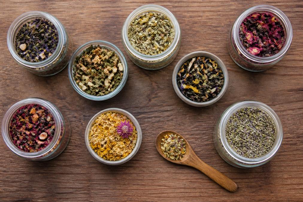 Overhead shot of loose leaf artisan teas in glass jars and bowls, displaying vibrant colors from dried botanicals, flowers, and herbs with natural lighting