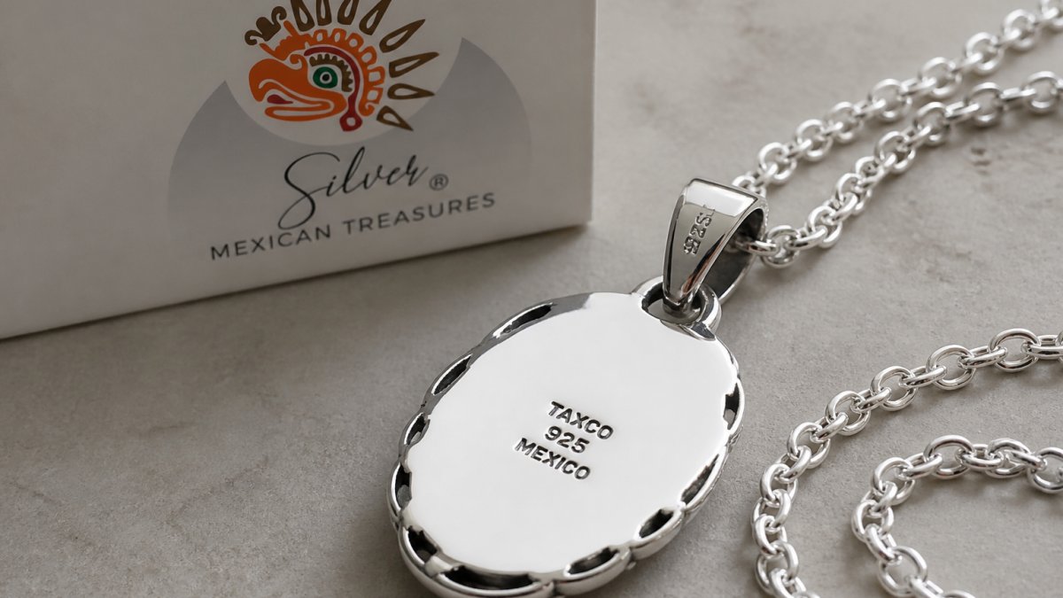 Close-up overhead shot of polished sterling silver pendant and chain on neutral surface, showing clear hallmark stamps and high-polish finish detail