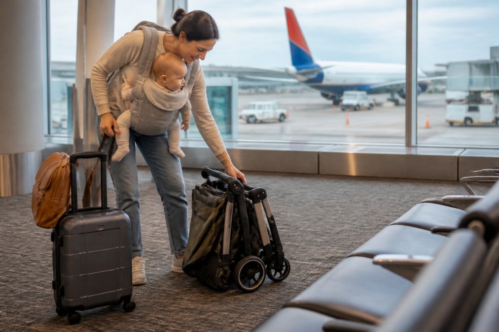 Parent folding a compact travel stroller at an airport gate, the best baby gear for travel 2026 for busy families.
