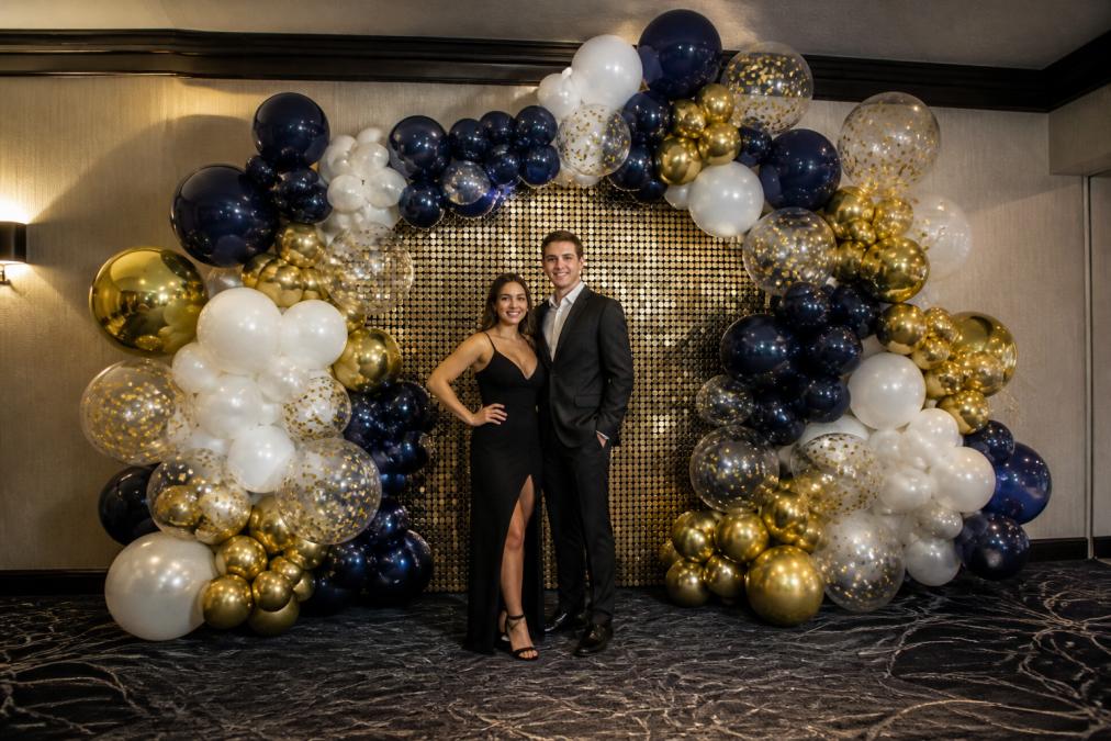 A completed balloon arch and backdrop installation at an indoor event venue, featuring a color-coordinated balloon wall with mixed sizes and a photo-ready setup with soft venue lighting in front of it
