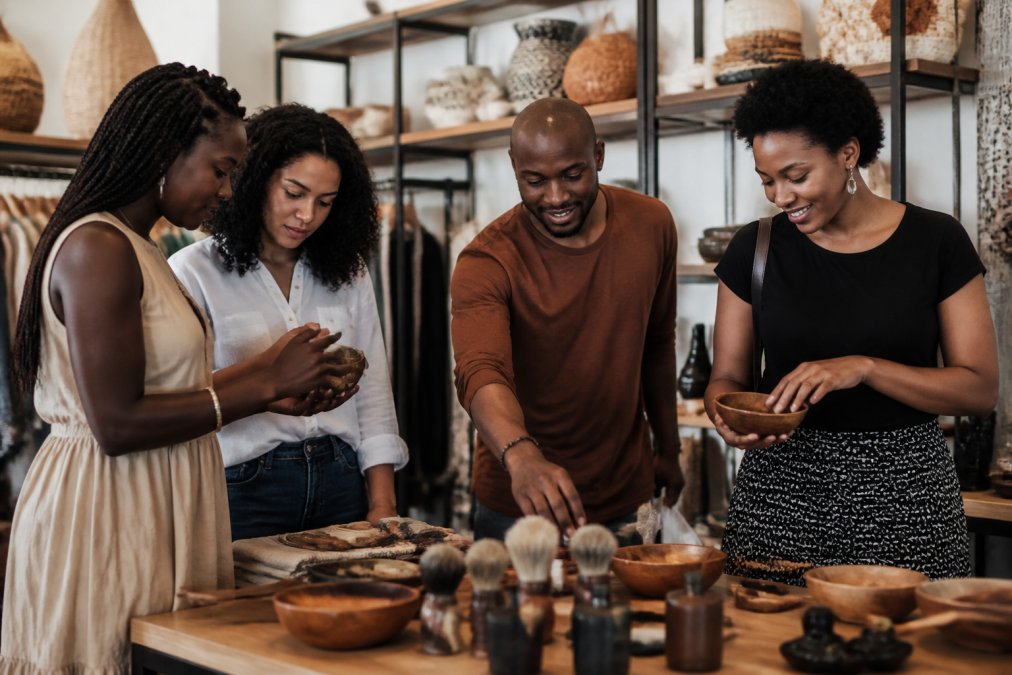 Diverse group of people shopping together in a vibrant retail space, examining artisan products and engaging with Black-owned merchandise displayed on wooden shelves and tables