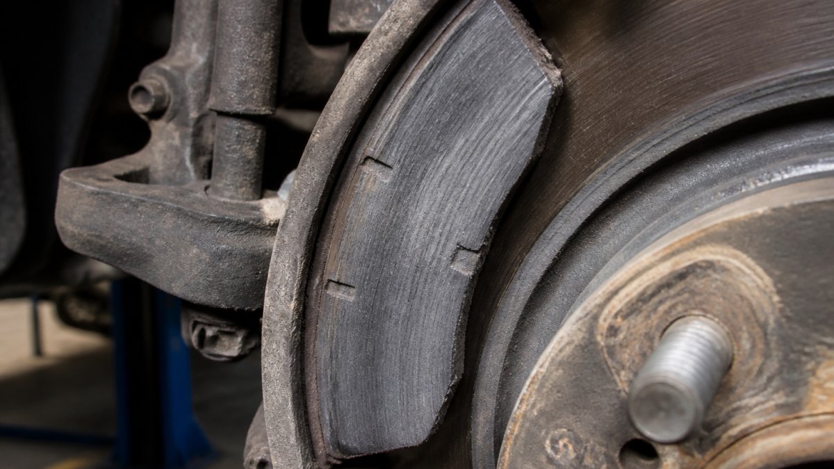 Close-up of a truck brake pad showing visible wear indicators, thin friction material, and dust buildup against the rotor in a professional service bay