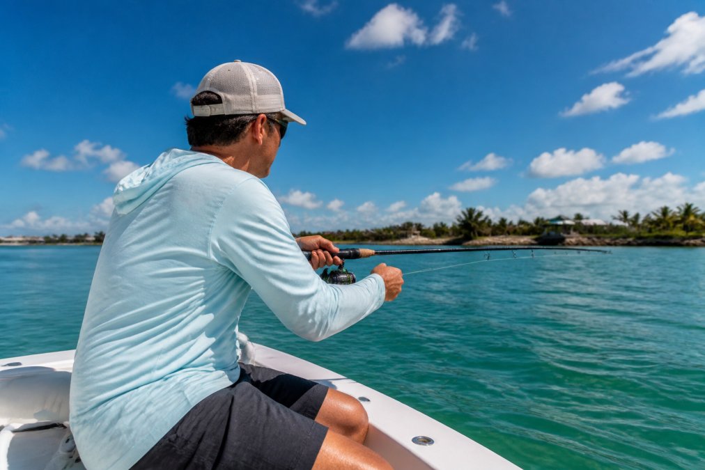Angler wearing breathable clothing casting a fishing line from a boat on a sunny day at sea