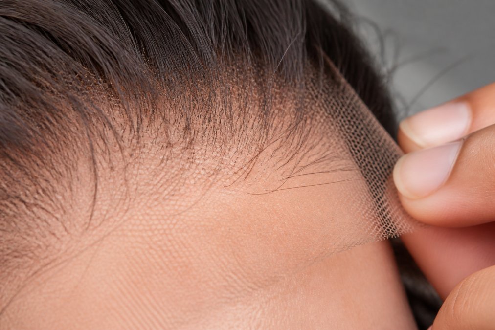 Close-up detail of Swiss lace mesh texture on wig cap showing fine hairline appearance and ventilation holes, photographed under bright studio lighting to reveal mesh structure