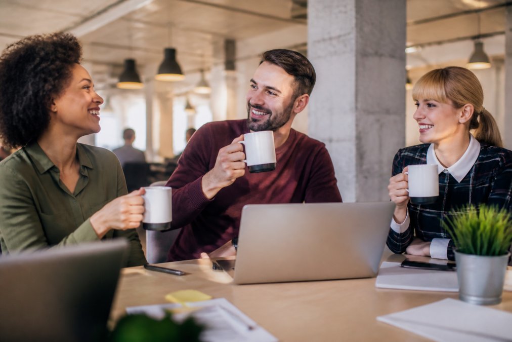 Team members in an office setting enjoying branded custom mugs at their desks, showcasing company logo prints and professional design quality