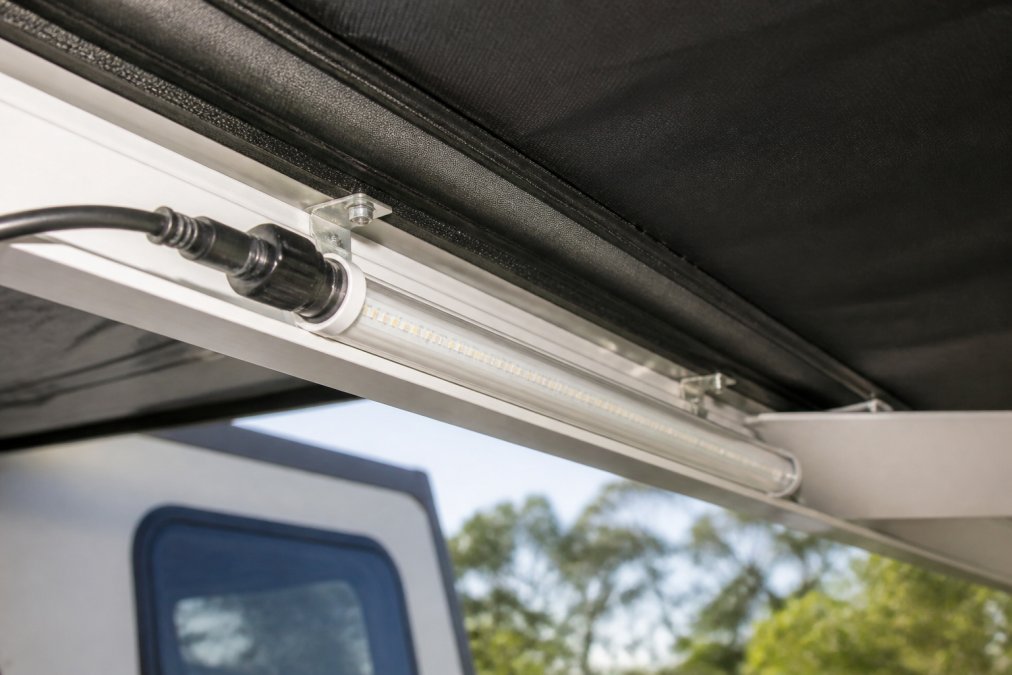 Close-up of a 12V LED strip light mounted on caravan awning frame with rigid aluminium housing and waterproof connectors, showing daylight reflection on the durable exterior casing