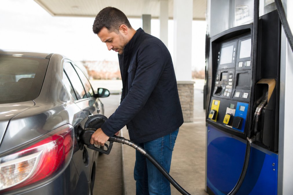 Person filling up a compact sedan at a gas pump with pump display visible showing fuel amount and price