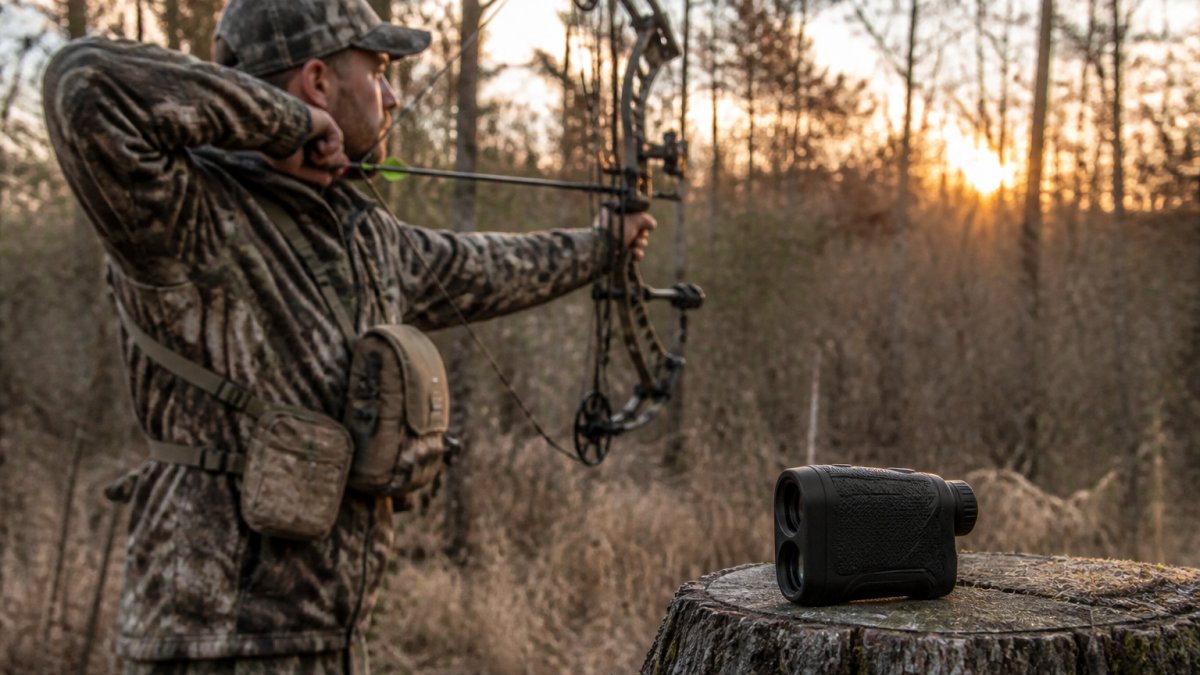 A bowhunter in camouflage drawing a compound bow in a wooded area at dawn, with a compact black rangefinder resting on a nearby stump