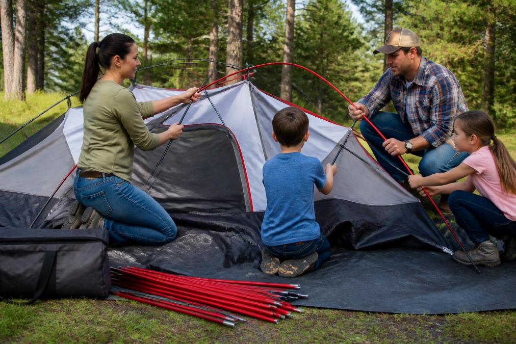 Family of four assembling one of the best camping tents for large families using color-coded poles in a sunny field.