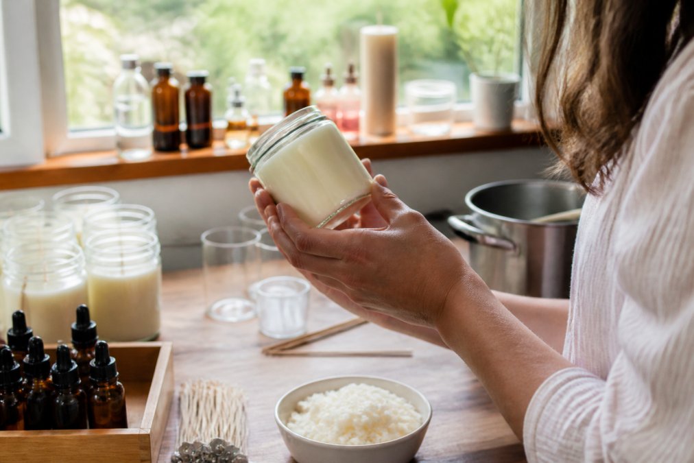 Close-up of hands holding a hand-poured scented candle jar, examining the fragrance label and scent notes in natural daylight from a window