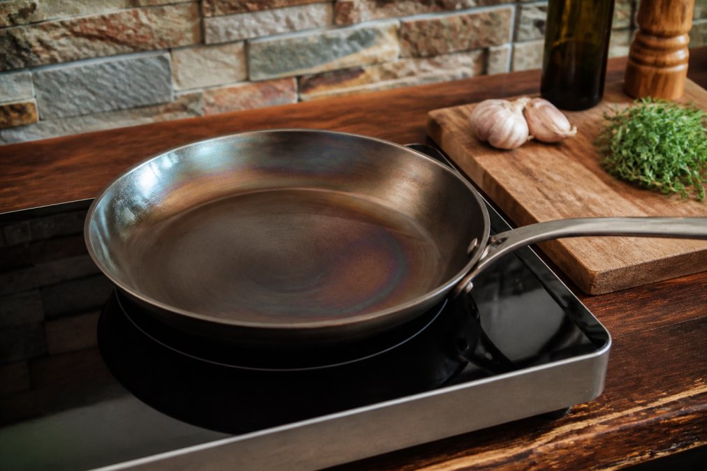 A carbon steel skillet sitting on an induction cooktop with a heat-distribution visualization overlay showing the hottest zone (red) directly above the burner coil and cooler zones (yellow, orange) toward the edges