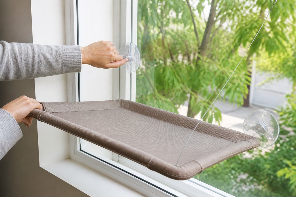 Hands demonstrating proper suction cup installation on a clean apartment window, showing firm downward pressure and the angle technique, with natural window light