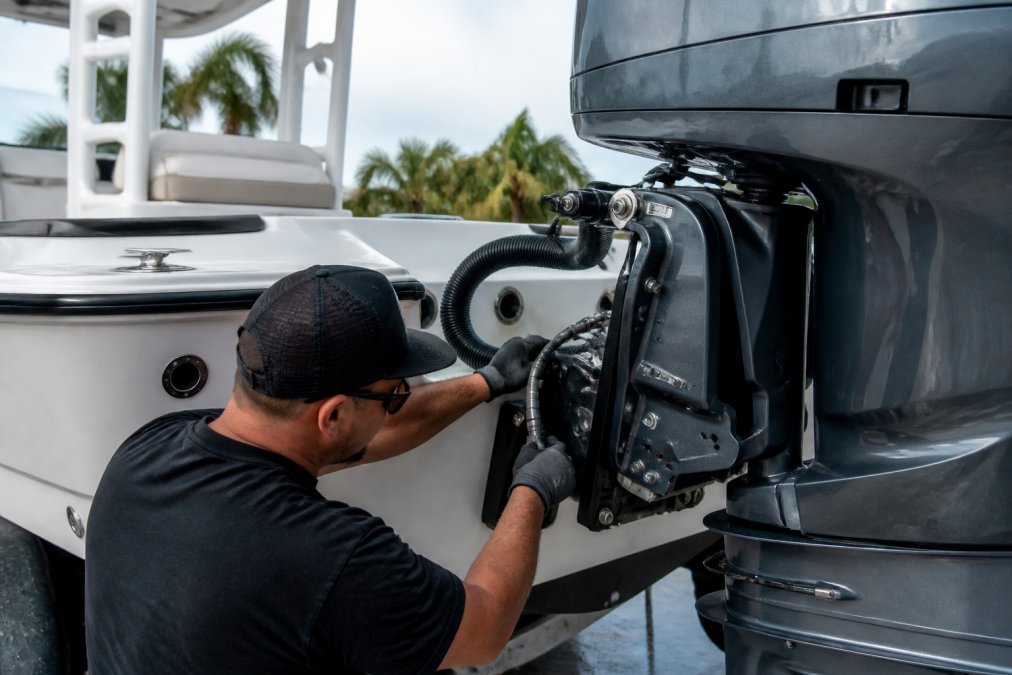 Professional marine technician installing new outboard motor on center console boat transom, showing engine mounting brackets, fuel lines, and electrical connections being secured