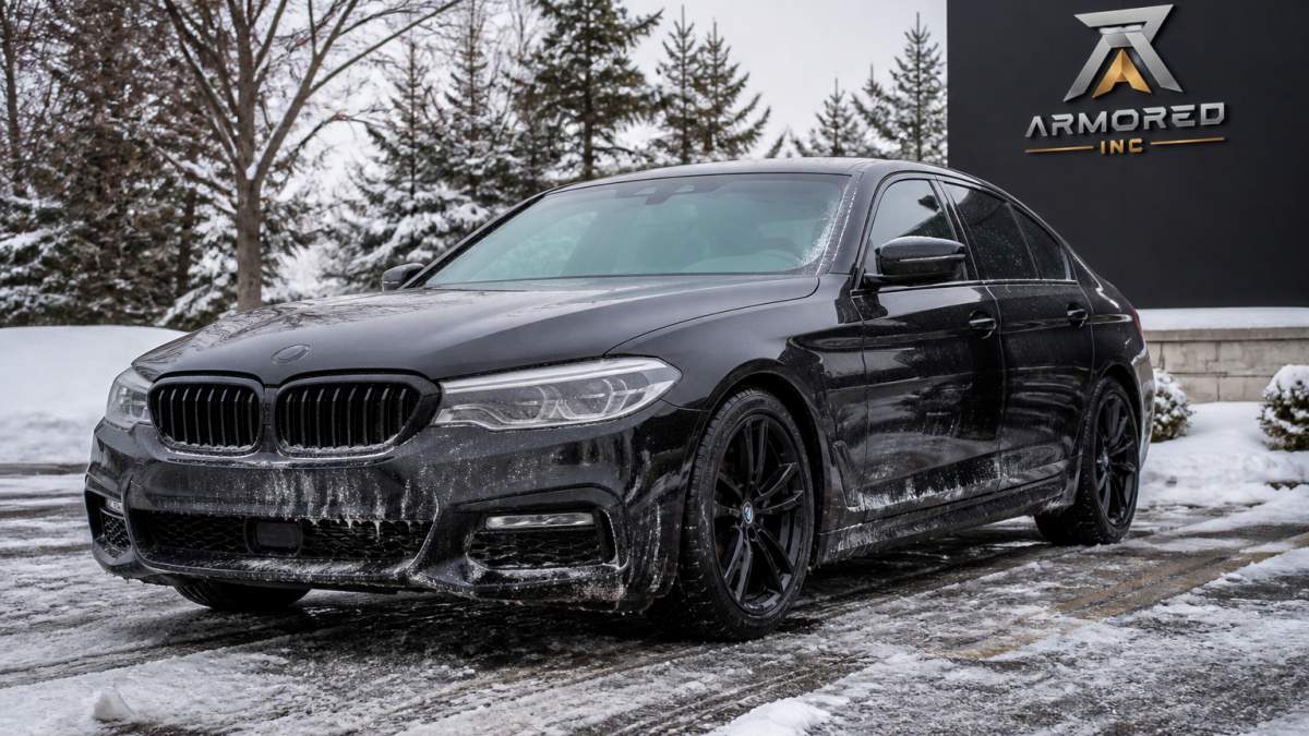 Luxury sedan parked in snow-covered parking lot with visible road salt residue and ice on pavement, winter trees in background