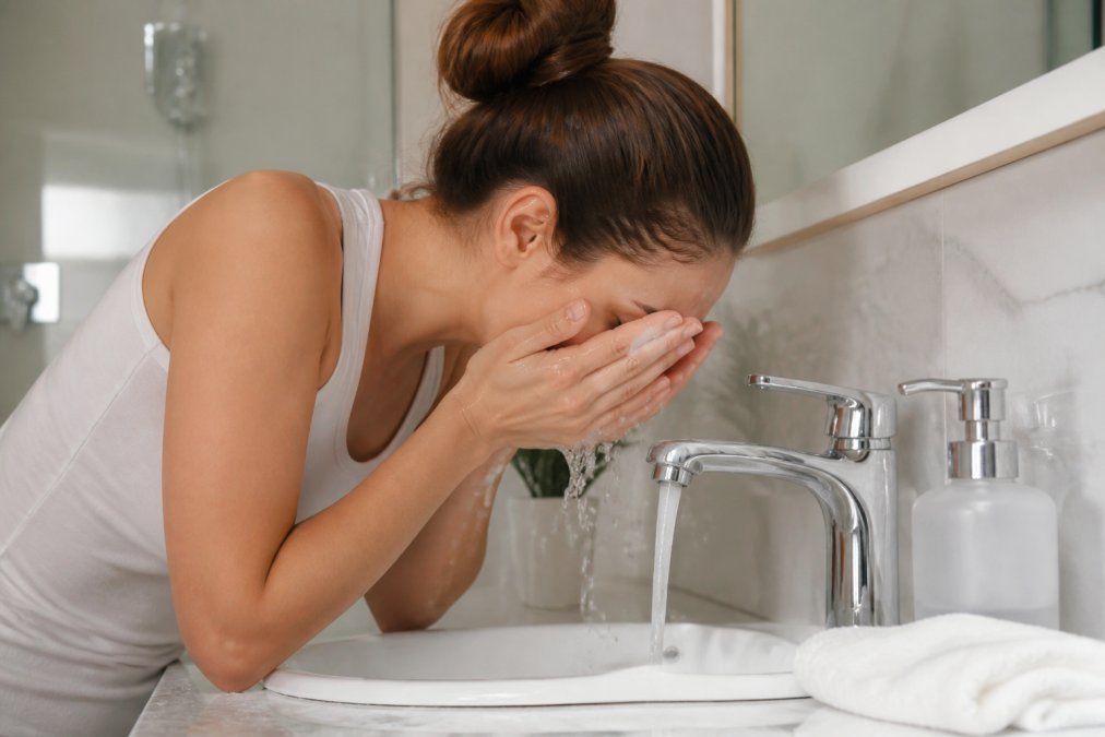 Person washing their face with gentle cleanser over a sink, showing proper pre-peel cleansing technique with warm water and a soft cloth