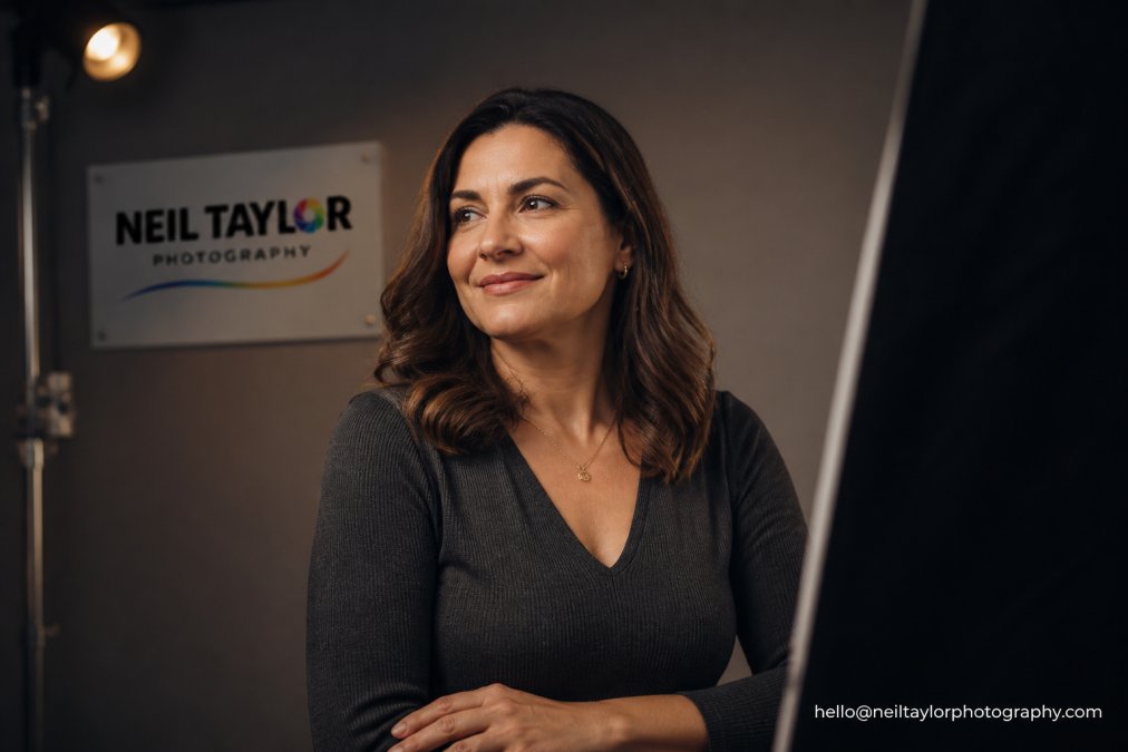Business professional wearing charcoal grey v-neck top with subtle texture and delicate jewellery, posed confidently against neutral studio background with warm lighting creating depth and colour harmony