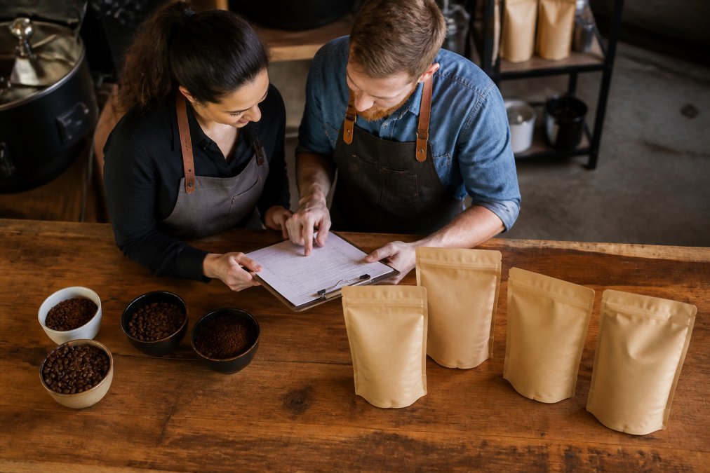 Cafe owner and roaster reviewing order details with the best coffee roasters for wholesale supply on a wooden counter