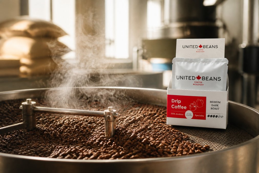 Close-up of freshly roasted coffee beans cooling on a metal tray in a bright roastery, steam rising, with roast date labels visible on the tray edge
