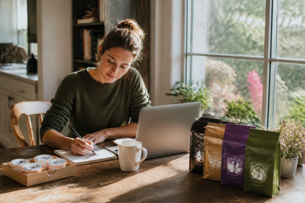 Remote worker at home desk with laptop, coffee mug, and notebook, morning sunlight streaming through window