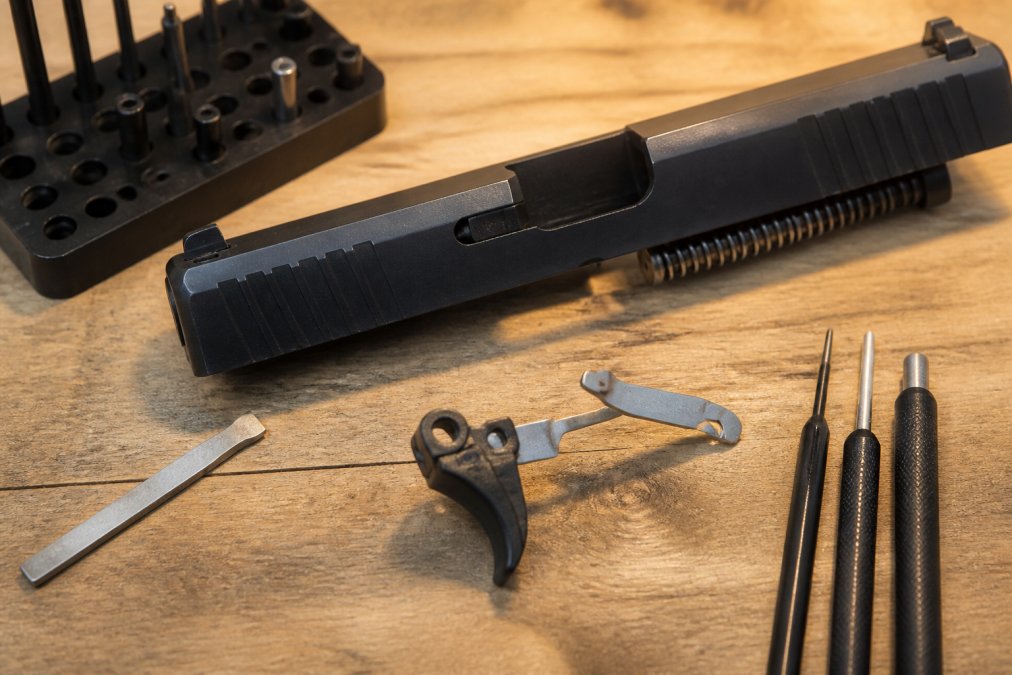 Glock slide and drop-in trigger unit on a workbench with tools for installing combat armory trigger alternatives