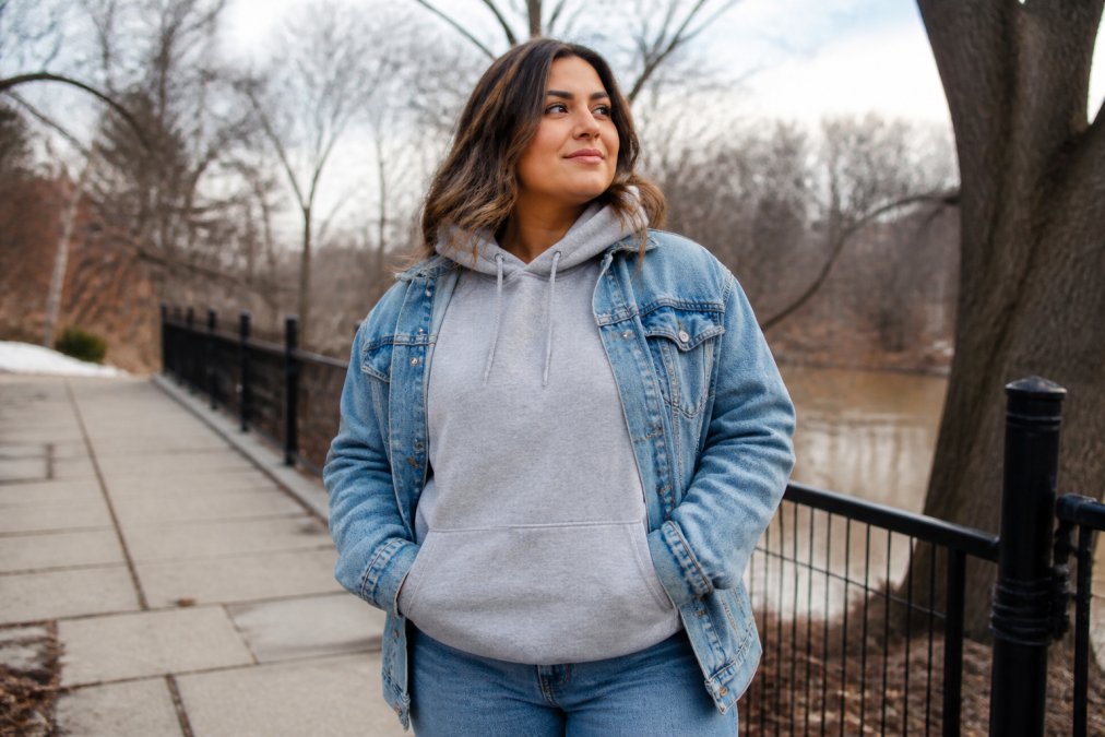 Woman wearing a comfortable faith sweatshirt layered with a denim jacket and jeans, standing outdoors in cool weather with a confident, approachable pose