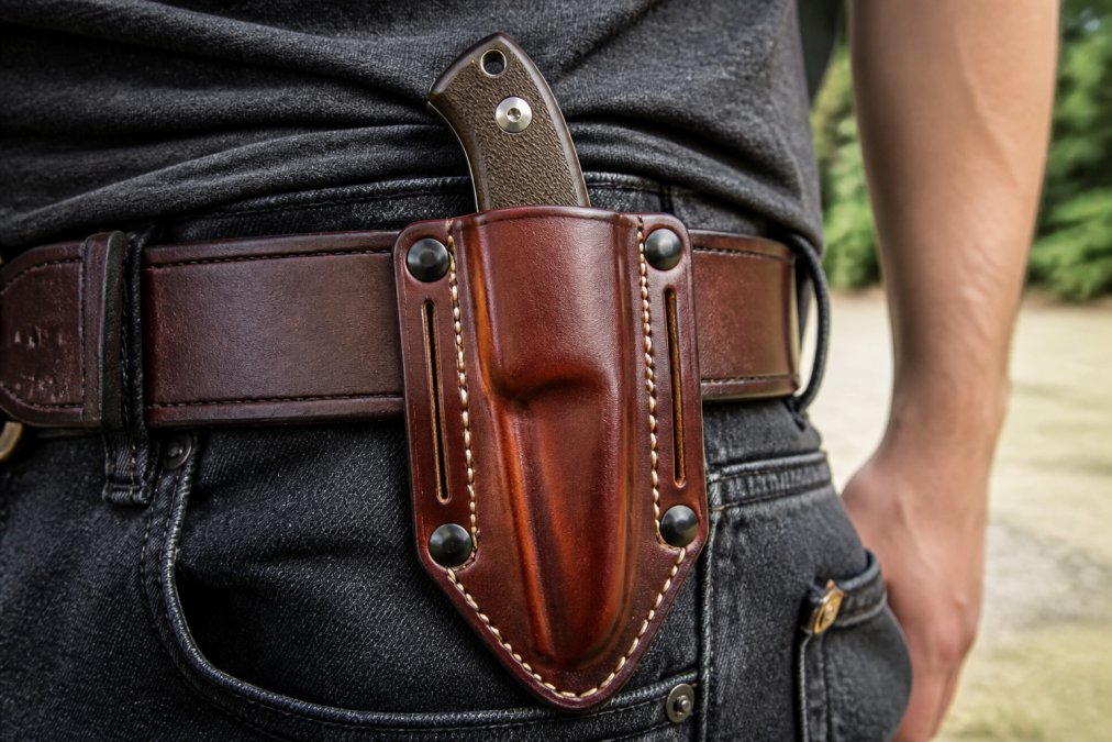 Handcrafted leather pancake sheath with detailed saddle stitching secured to a brown belt in natural daylight