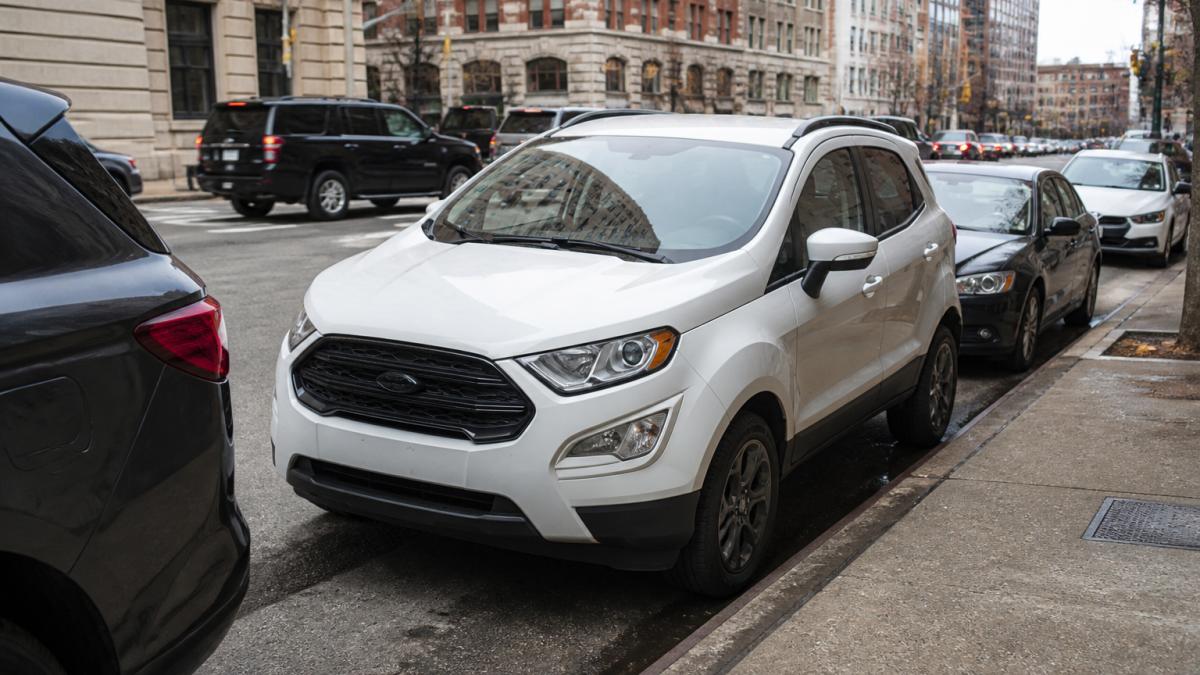 Compact SUV parked on a tight urban street with buildings and city traffic visible in the background, showing tight parking space and urban density