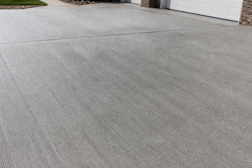 Close-up of broom finish concrete driveway surface showing subtle parallel ridges and uniform texture created by brush strokes, photographed in natural daylight
