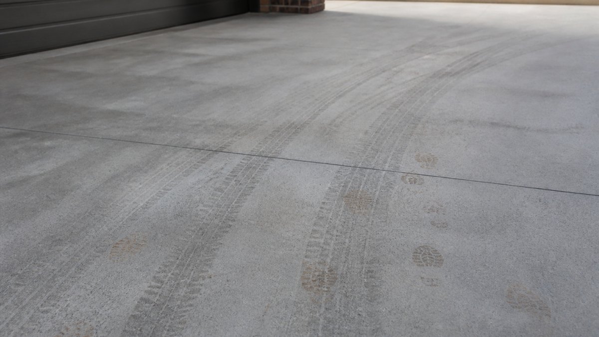 Close-up of a driveway surface with fresh concrete overlay showing tyre marks and footprints, demonstrating traffic resistance under natural daylight
