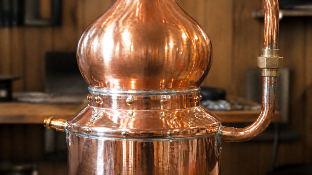 Close-up of a handcrafted copper still with polished surface, showing rivets and lead-free solder joints in a workshop setting