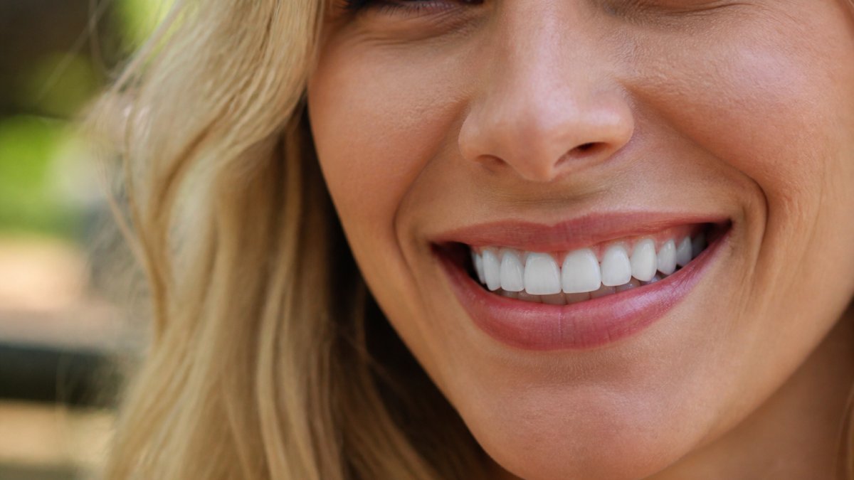 Close-up of a person smiling confidently with bright, even teeth showing natural-looking porcelain veneers in natural daylight