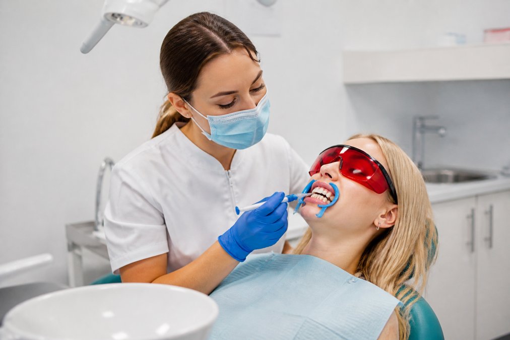 Patient receiving professional teeth whitening treatment in modern dental surgery with dentist applying whitening gel under bright clinical lighting
