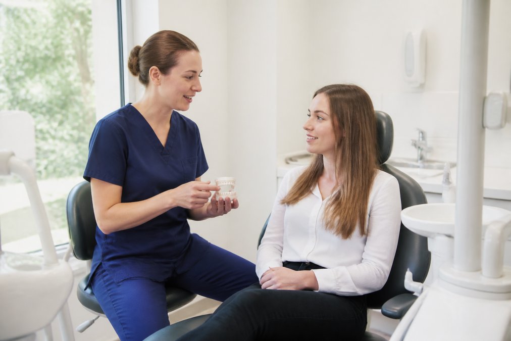Dentist in professional attire consulting with patient in modern, bright dental surgery with comfortable seating and natural lighting