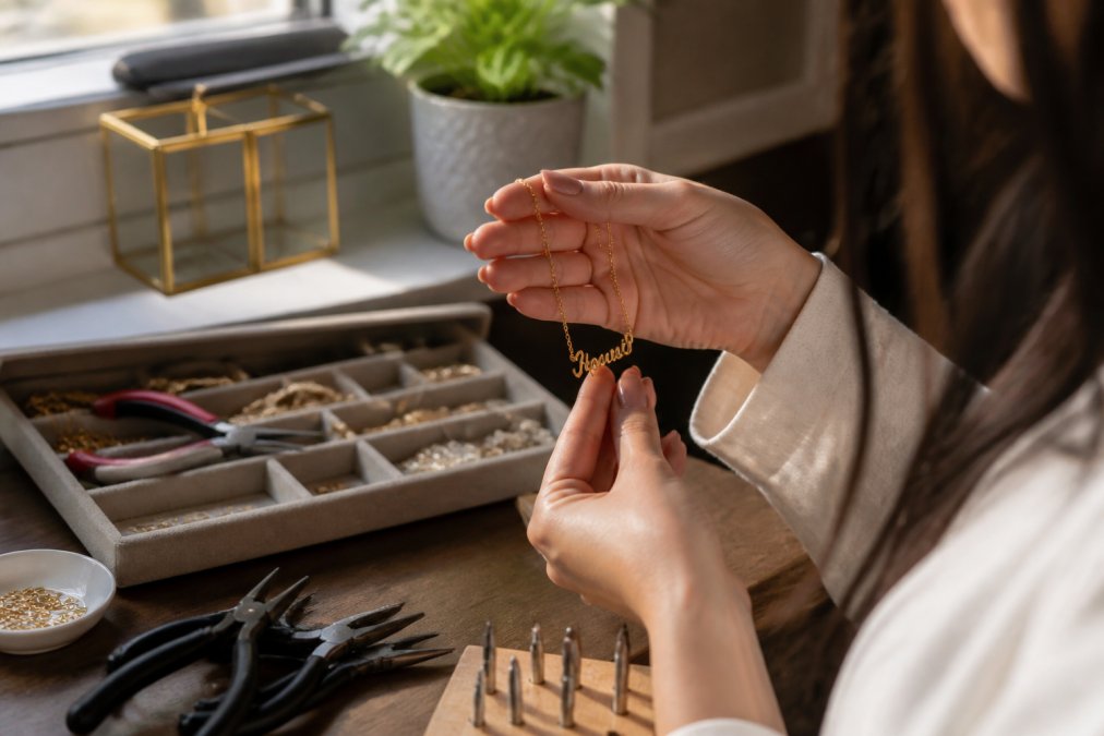 Close-up of a woman's hands examining a personalized necklace with an engraved name, holding it up to the light to inspect the craftsmanship and metal finish in natural sunlight