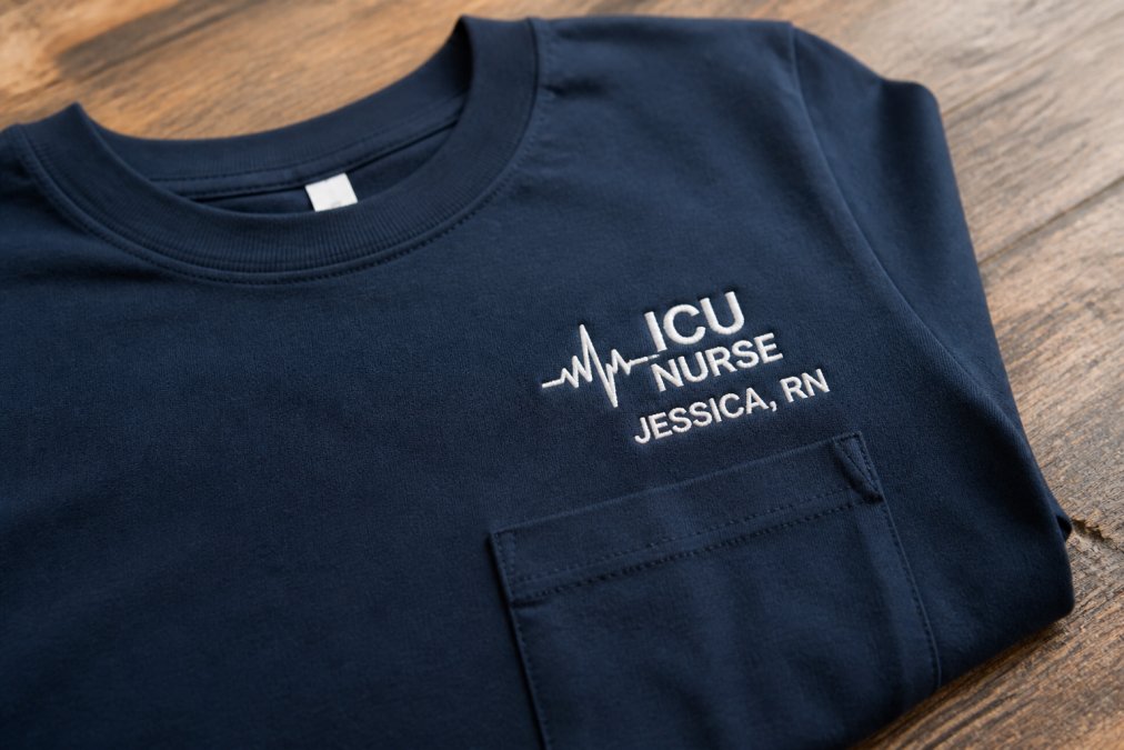 Close-up of a custom nursing t-shirt laid flat showing embroidered department name and personalized details on the chest with professional lighting