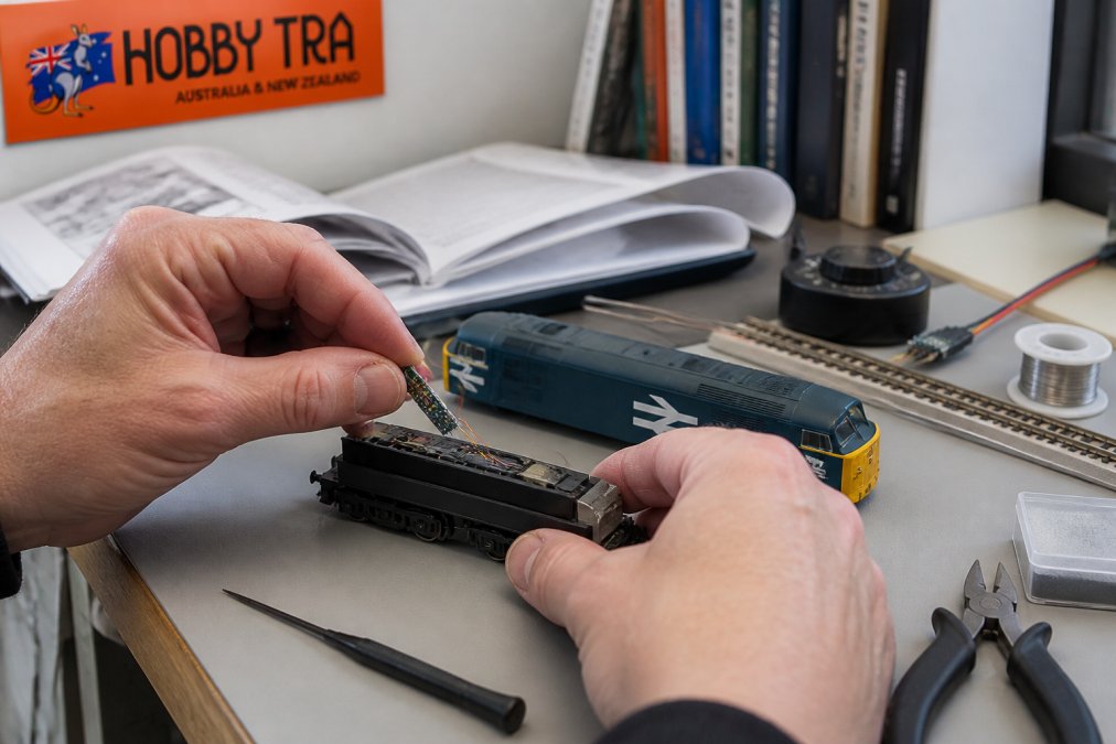 Modeller installing a DCC train control decoder into an HO scale locomotive on a workbench