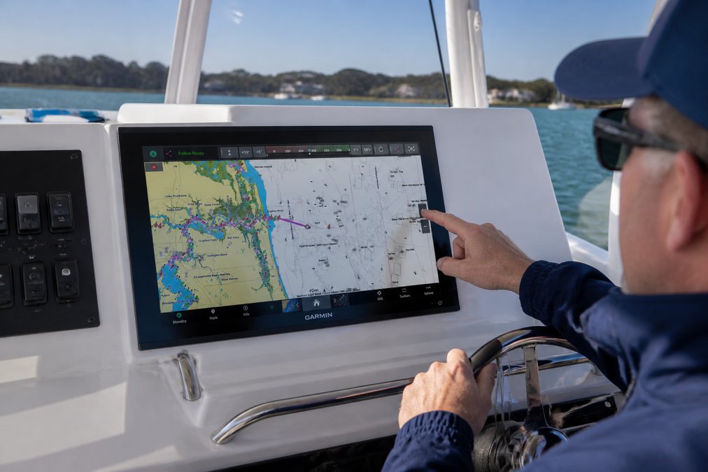 Boat captain's hands adjusting multiple integrated Garmin displays and control panels on a modern helm, showing NMEA 2000 networking cables, transducer connections, and real-time data across multiple screens in bright daylight
