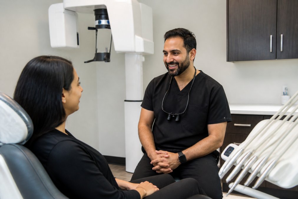 Board-certified dental specialist in clinical attire consulting with a patient in a modern treatment room equipped with advanced cone beam scanner and state-of-the-art dental instruments