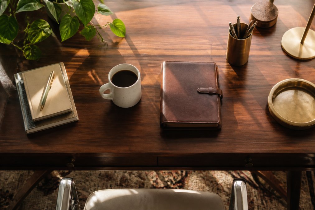 Polished wooden executive desk featuring elegant desk accessories like a brass pen holder, leather notebook, and mug.