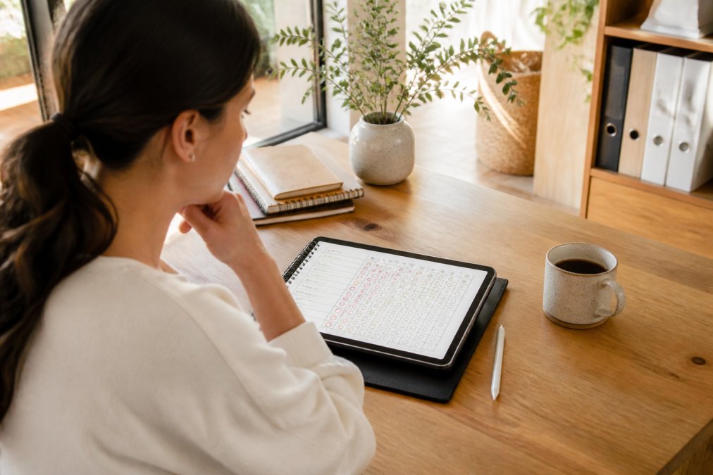 Person using a habit tracking app on a tablet with digital planners at a tidy desk with coffee
