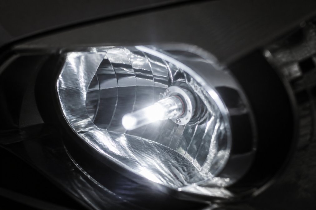 Close-up of an LED headlight bulb glowing with bright 6500K white light installed in a vehicle headlight housing, showing the crisp beam pattern against a dark background