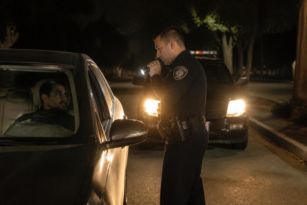 Police officer conducting a traffic stop at night with vehicle headlights visible, showing the moment of initial law enforcement interaction