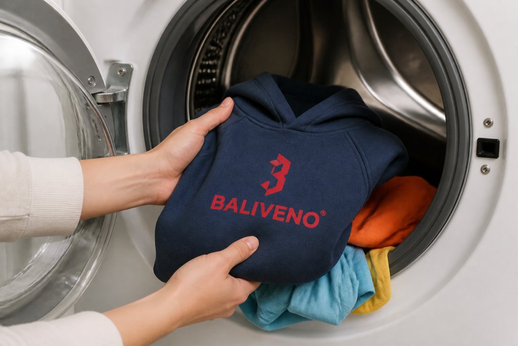 Close-up of hands loading colorful children's clothing into a washing machine, showing proper garment handling with gentle placement