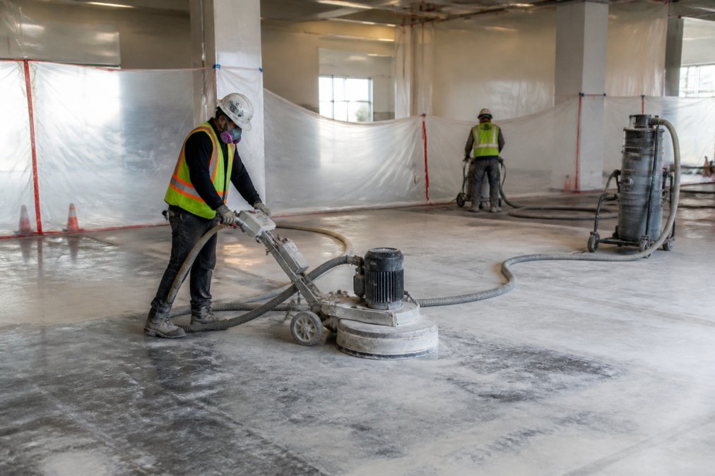 Professional crew performing surface preparation on concrete retail floor with grinding equipment and workers in safety gear, dust containment setup visible