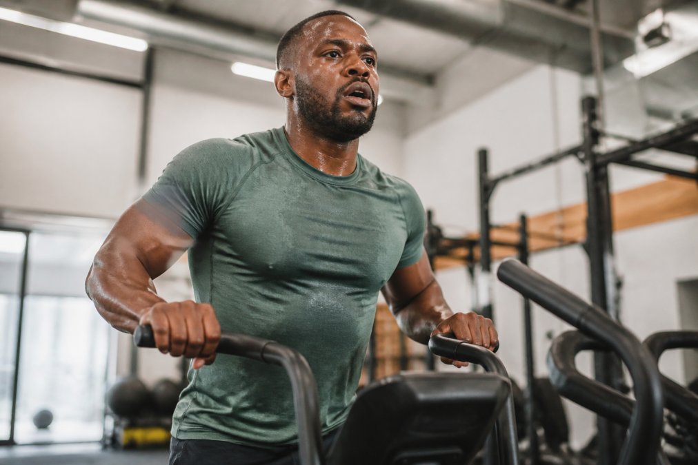 Athlete wearing moisture-wicking bamboo fabric apparel during intense cardio workout, sweat visible on chest and shoulders, fabric clinging to body showing breathability, bright gym lighting