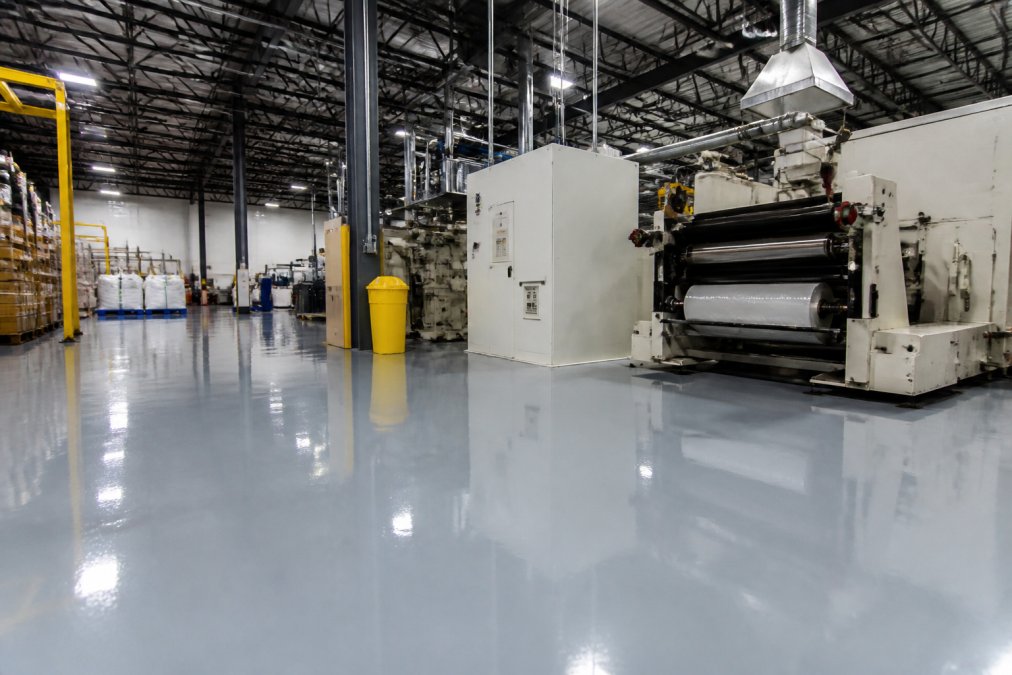 Warehouse floor with heavy industrial machinery and equipment positioned on a glossy epoxy coating, showing the durability and resistance to chemical spills in a well-lit industrial environment