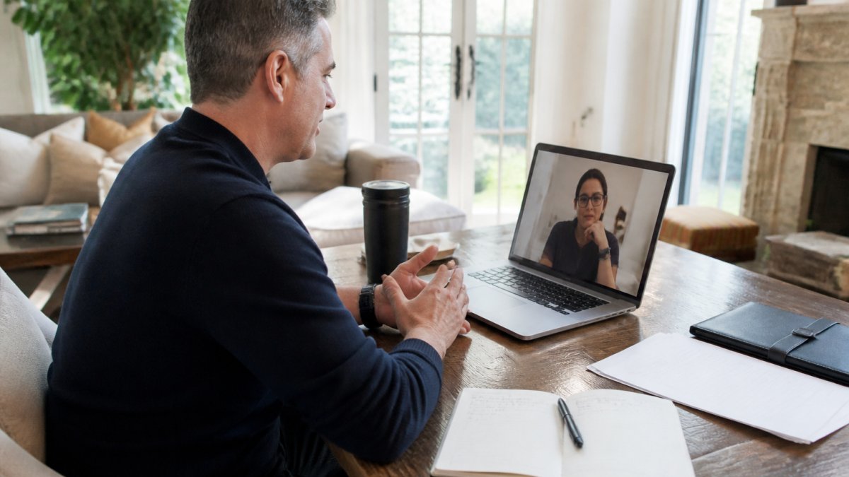 A senior executive in a video call with a coach, laptop open with notes and a leadership resume on the desk in a bright home office
